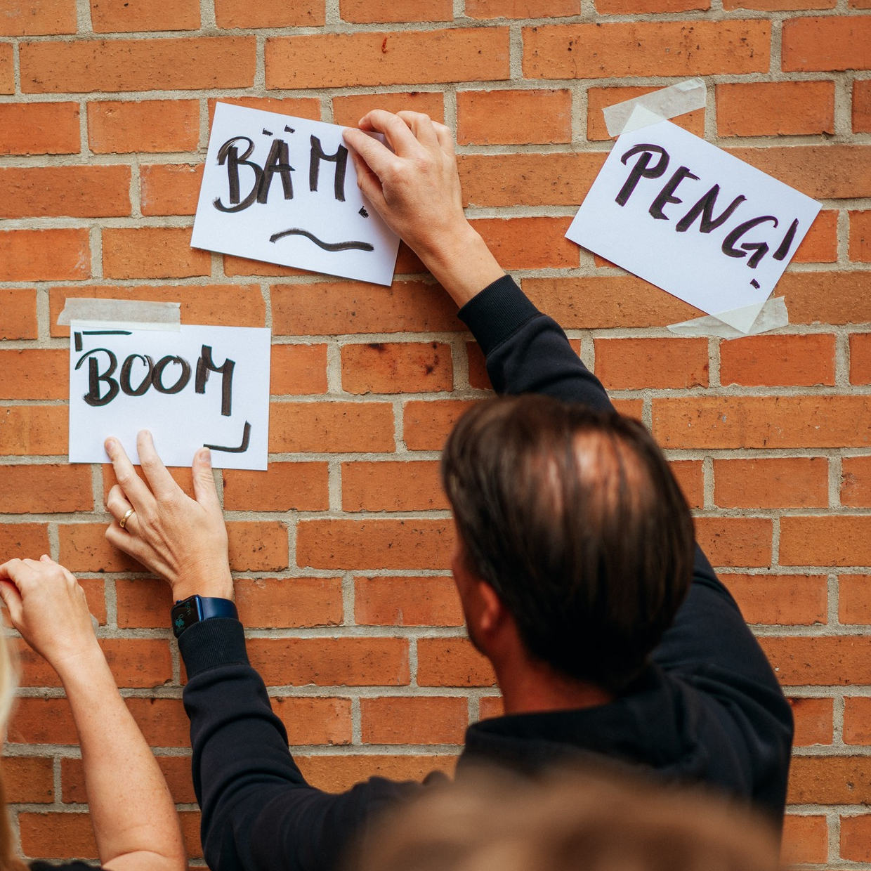 Eine Person hängt weiße Zettel an eine Backsteinwand, auf denen handschriftlich 